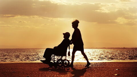 Un homme en fauteuil roulant poussé par une femme sur une plage